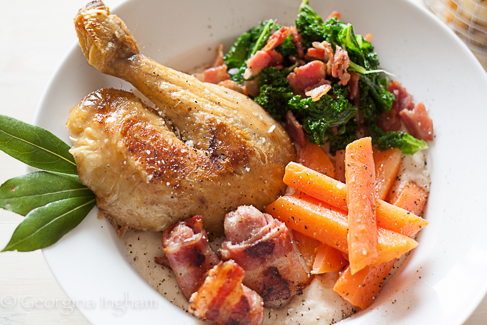Portion of lemon and herb roast chicken served with buttery carrots, kale with bacon and gravy.